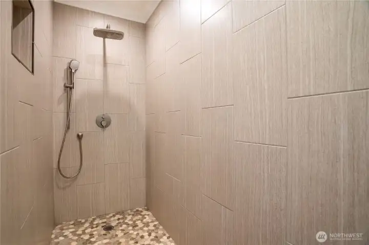Spa-inspired walk-in shower featuring a ceiling-mount rain head, hand-held wand, designer brushed nickel fixtures, and stunning pebble stone mosaic floor — a true daily retreat.