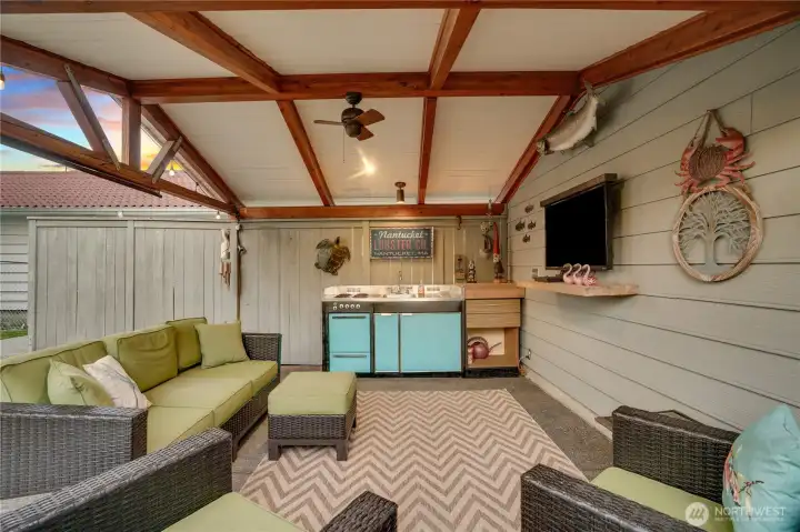 A fully equipped outdoor room — ceiling fan, mounted TV, vintage camp kitchen, and a vibe you can’t buy at a furniture store. It all stays.