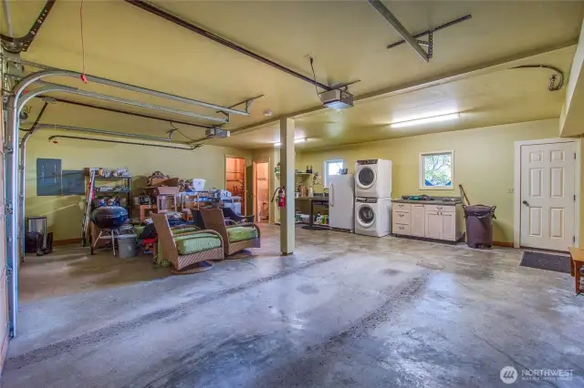 The oversized garage contains two mechanical rooms, a built-in workbench (on left, covered with personal belongings), a sink, freezer, laundry center and cabinetry. Door leads to stairs to the deck