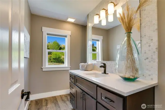 Luxury awaits in the main floor powder room with a generous vanity, quartz countertop, full tile backsplash and luxury vinyl flooring.