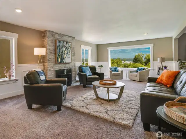 The spacious living room offers ample space for entertaining, featuring a wood-burning fireplace ideal for cozy Northwest evenings. Take note of the lighting, the fully wood-wrapped windows and trim, and the elegant chair rail and wainscoting details.