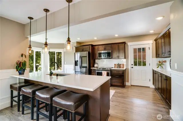This timeless kitchen offers features to admire including quartz countertops, soft-close cabinetry, stainless steel appliances, and a subway tile backsplash. The door visible in the space leads to the second view deck, perfect for barbecuing and entertainment.