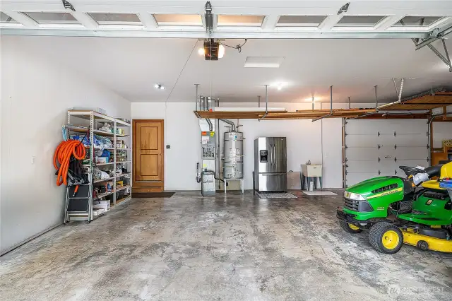 Massive 4-car garage with pass-through garage in the back right. Riding mower included! The kitchen is on the back left. Second refrigerator/freezer provides space for beverages, holiday leftovers, and more. Note the racks hanging from the ceiling; they provide additional storage space for seldom-used items. The shelving on the left of the door will stay.