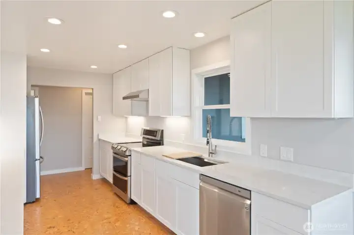 Bright kitchen with double ovens and stainless steel appliances, featuring a window that overlooks the deck and stunning views. The door across the hallway is a walk-in pantry.