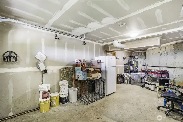 Basement unfinished storage area or workshop, with a small garage door as access to exterior.