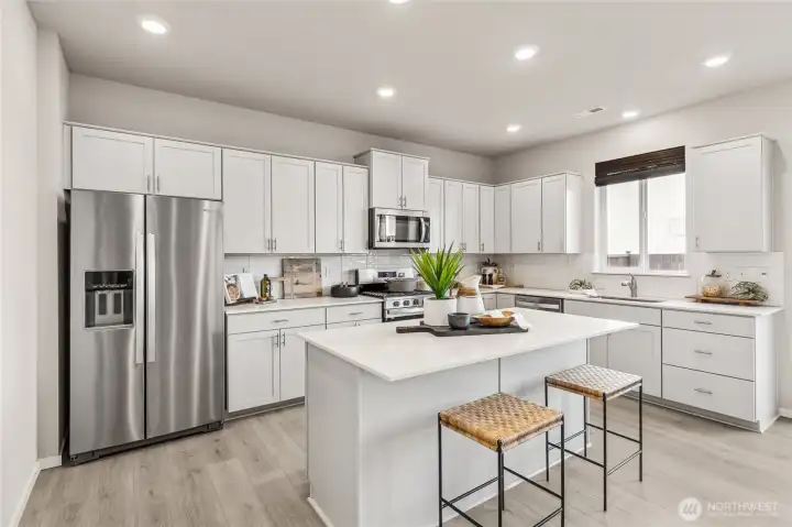 Modern gourmet kitchen featuring shaker style cabinetry, stainless steel appliances and quartz countertop island with bar seating.Photos are representative only and may display different color package and/or upgrades.