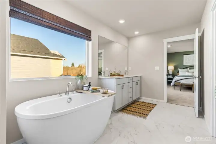 Primary ensuite bathroom featuring a freestanding soaking tub, oversized window with natural light, tile flooring, and a seamless connection to the primary bedroom. Photos are representative only and may display different color package and/or upgrades.