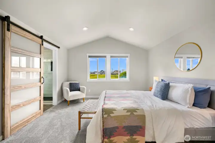 The spacious primary suite provides a peaceful retreat with vaulted ceilings, soft natural light, and a sliding barn door leading to the ensuite bath.