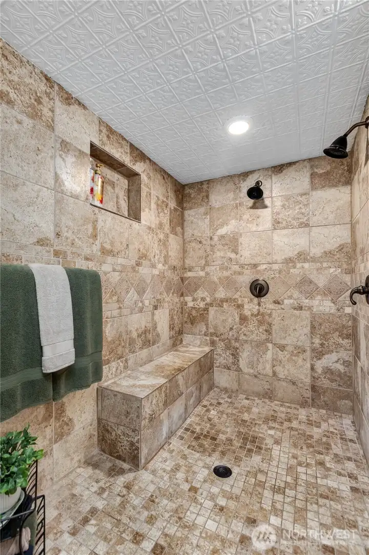 “Primary bathroom shower featuring dual showerheads and a built-in bench seat.” “Primary bathroom shower featuring dual showerheads and a built-in bench seat.”