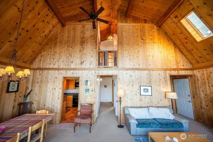 Vaulted ceilings and cozy cabin vibes from the wood paneling. Main floor, looking toward kitchen on the left, hallway in the middle, side entrance on the right