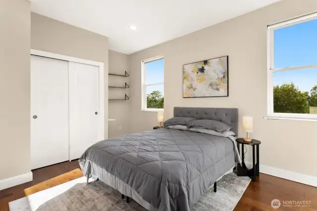 Sunlit and serene, this versatile bedroom offers peaceful views, hardwood floors, two spacious closets with organizer systems, and stylish shelving.