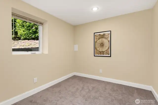 Tucked away downstairs, this bonus room offers a quiet retreat with soft carpet, recessed lighting, and a sunny window.