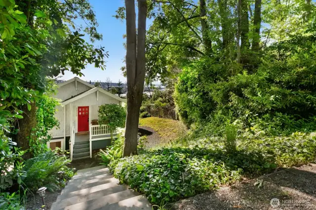 Tucked into a lush, tree-lined hillside, this inviting cottage welcomes you home with a bold red door, charming front porch, and a peaceful sense of privacy just steps from the city.