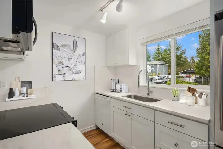 The roomy bright kitchen includes a south facing window, all new cabinets, kitchen appliances plus quartz countertops in the totally upgraded space.  Staging in this image is virtual.