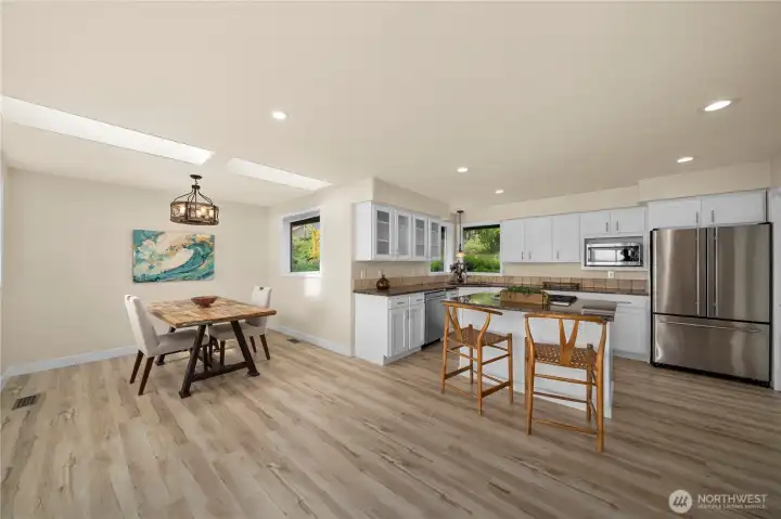 Open concept kitchen flows into the dining area, bathed in natural light from the skylights above.