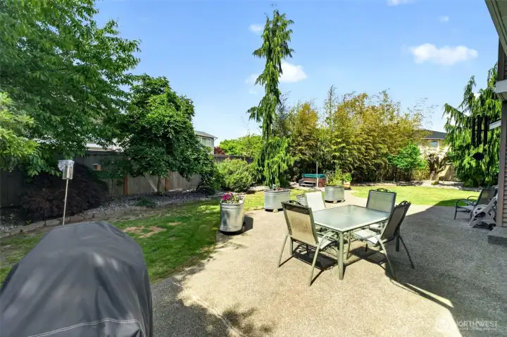 A large backyard with an extended aggregate backyard patio, sprinkler system, shed and garden beds