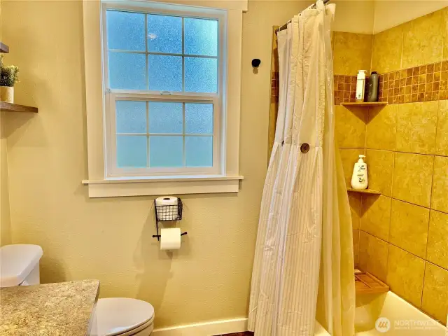 Country-style bathroom with a white-trimmed window, a tiled bathtub, and plenty of natural light, creating a bright and airy space with a charming, rustic feel.