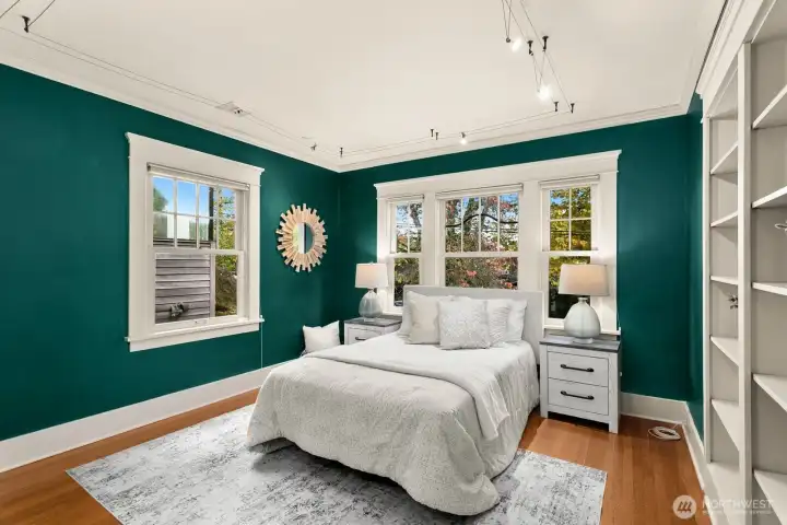 A main floor bedroom with deep green walls, abundant windows, and built-in shelving overlooking the garden’s changing colors.  Don't worry, there is a walk in closet here too.