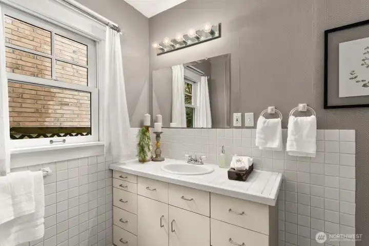 A crisp, classic bath with tiled walls, bright natural light, and timeless simplicity—beautifully maintained and ready for guests.