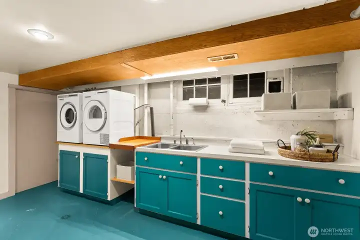 A cheerful, functional laundry room with a deep utility sink, storage space here with the cabinets, generous counter space for folding or crafts and even more storage on the opposite wall not seen in this photo.