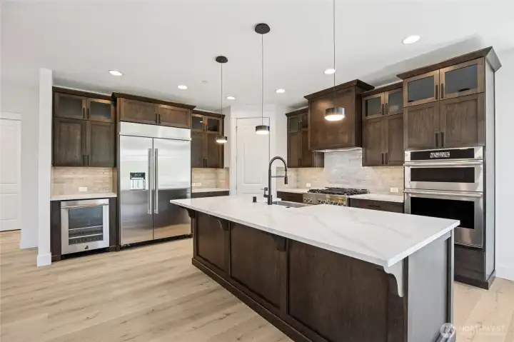 A chef's kitchen with JennAir appliances, pantry, double oven and gas range, beverage fridge, quartz counters, and Huntwood cabinets. Warm, yet bright and inviting.
