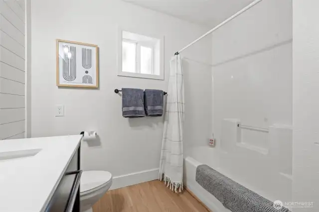 This bright, neutral bathroom is beautifully balanced with white fixtures, soft wood accents, shiplap walls and designer lighting