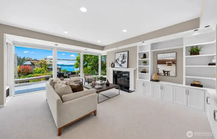 A gas fireplace with custom white built-ins anchors one wall while a wall of floor-to-ceiling windows frame Lake Washington and the deck beyond — two focal points that make this living room impossible to leave. Hunter Douglas motorized shades sit discreetly above each window, giving you full control of the light without ever sacrificing the view.
