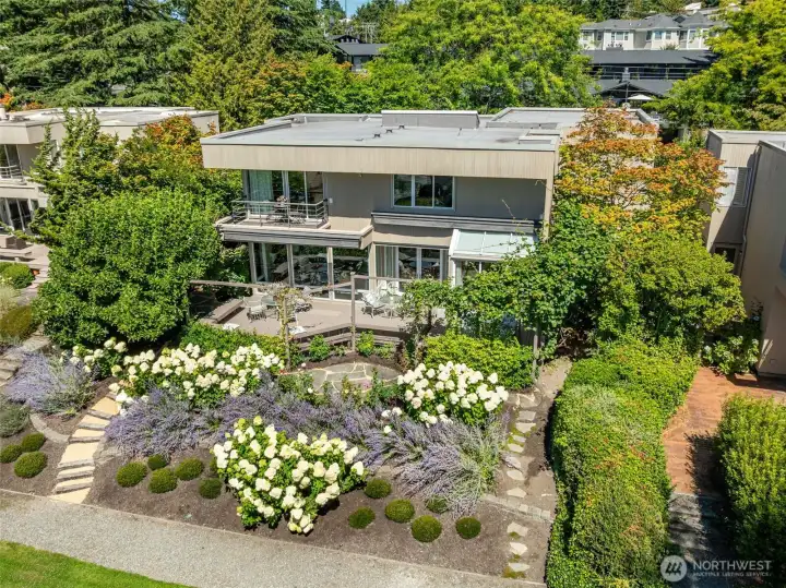 The full rear elevation reveals the true scale   of this outdoor living space — the primary   suite balcony above, the main level deck   below, the glass breakfast room conservatory   to the right, and Ohashi's sweeping garden   beds tying it all together in a setting that is   unmistakably Lochleven.