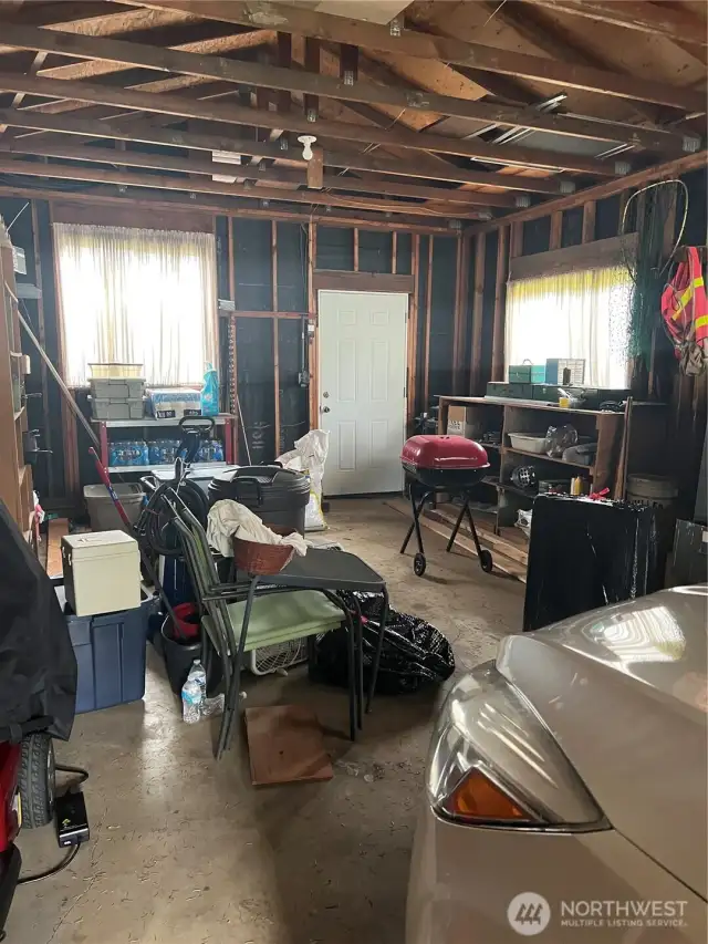 Half of the garage is shop with access door in the back.  Workbench and floor to ceiling shelving on left side of photo...