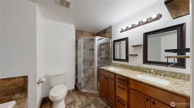 Ensuite primary bath with walk-in closet and a 5-piece bath with soaking tub, tile shower, double vanity, granite counters, and tile floors