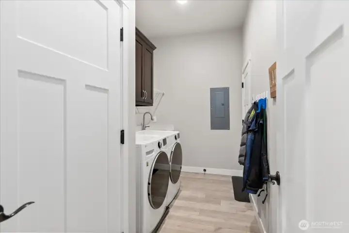 Laundry room features sink and vanity. Door  to the left is utility closet and furnace. Door  next to the panel leads out to the garage.