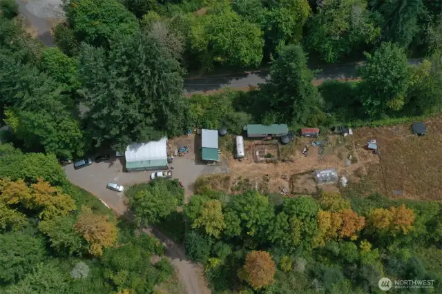 Parking area, 2 cargo containers with industrial roof spanning space between, the shed quarters, a cargo container with electricity and a "bedroom" with garden area in front, greenhouse. The line of trees indicates the creek.