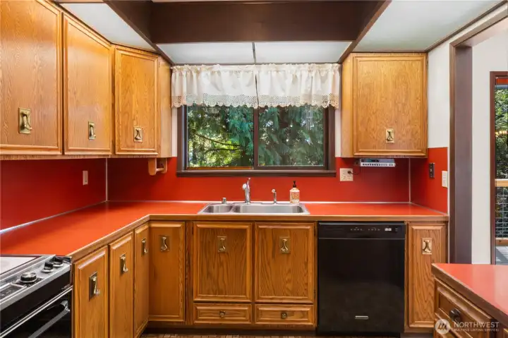The original kitchen has wood cabinets, overhead lighting, a view from the sink, and appliances that just keep on working!