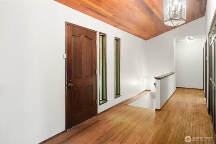 The front entry has real hardwood floors and vaulted wood ceilings. A row of closets are on the right, and the stairway to the daylight basement is in the foreground.