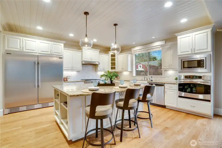 A stunning chef’s kitchen featuring gleaming stainless-steel appliances, a six-burner cooktop, double-door refrigerator, built-in microwave, and classic farm sink. The expansive island offers additional seating, while the subway tile backsplash and elegant granite countertops add the perfect finishing touches.
