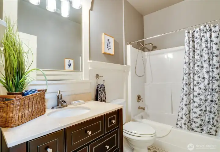 Even the main floor bathroom boasts high-end touches, featuring tile flooring, a vanity with granite countertops and ample storage, charming beadboard details, and a beautifully trimmed mirror.