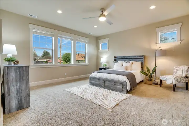 This dreamy primary suite boasts abundant windows that flood the space with natural light, freshly cleaned carpets, recessed lighting, and a ceiling fan to keep things cool on warm summer nights, creating a spacious and relaxing retreat.