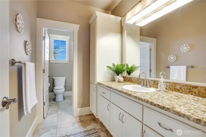 This upstairs main bathroom has tile floors, a timeless granite countertop, plenty of storage, and a fully trimmed accent around the mirror. It also includes a separate bathtub with a shower and a toilet for extra comfort and convenience.