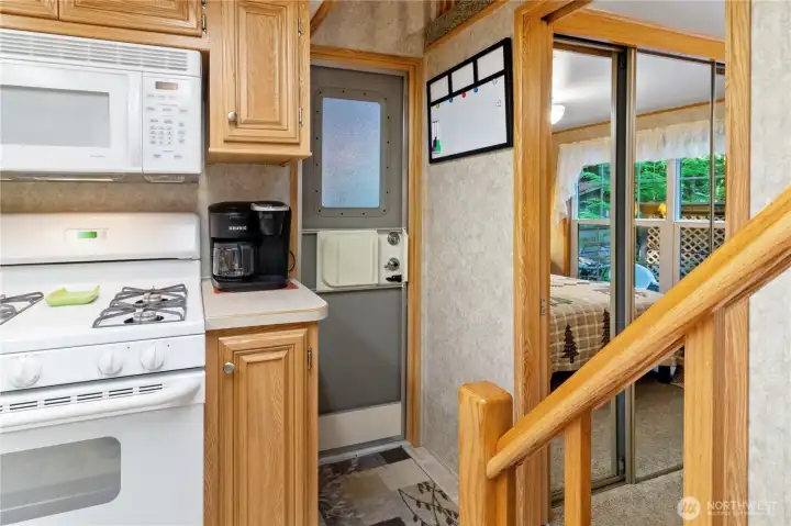 Kitchen area w/ range, microwave & cabinetry. Stairs to loft near entry.