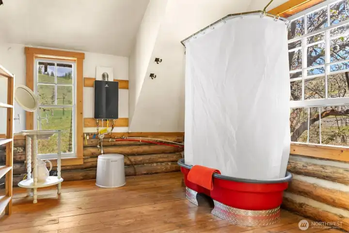 Loft ensuite Shower room has freestanding vanity wash basin with pitcher. Shower. On-demand propane hot water heater on wall. Rustic wood floors. Shelf system for personals.