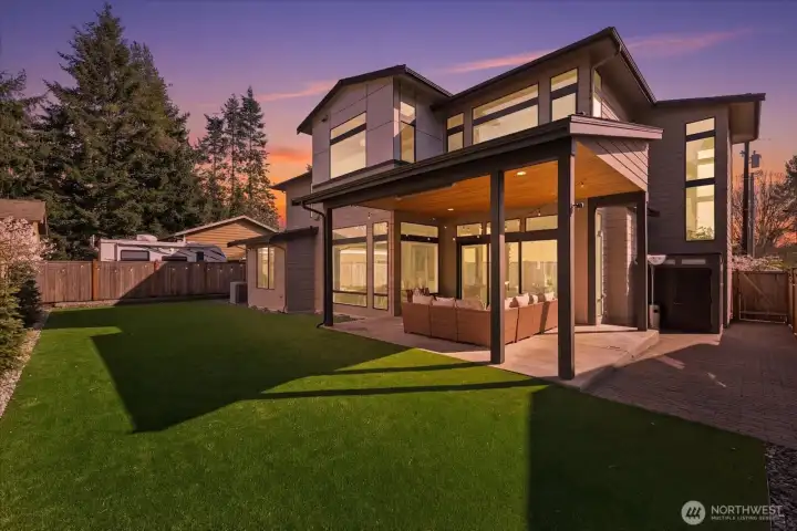 As evening falls, the covered outdoor living space becomes a private Kirkland retreat with Infratech heaters, designer lighting, premium turf, and a low-maintenance backyard made for year-round entertaining in North Rose Hill.