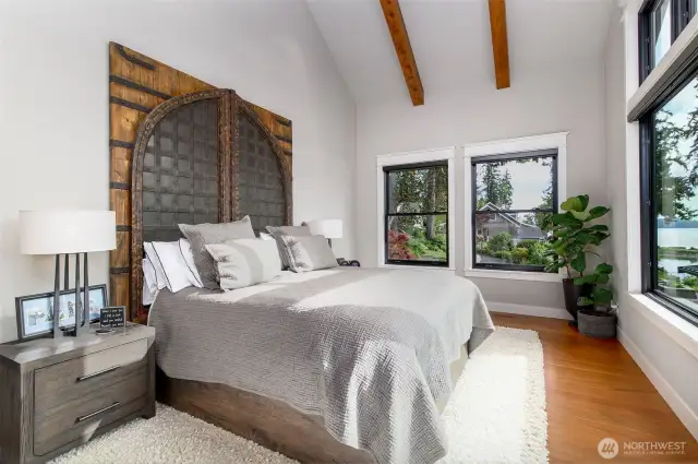 The private wing of this Puget Sound waterfront estate, where the primary ensuite is a sanctuary of style and comfort. A striking, arched headboard anchors the room, while floor-to-ceiling windows invite natural light and frame serene water views. Vaulted ceilings with rich wooden beams add a touch of grandeur, ensuring this space is your personal haven for relaxation and rejuvenation.
