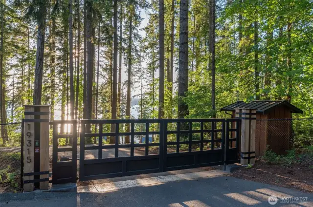 The grand security gate entry to the private waterfront estate, offering a glimpse into a secluded and luxurious retreat. The robust, elegant custom designed gates stand as a promise of privacy and exclusivity, opening to reveal a lush, tree-lined drive that leads directly to the water's edge. This entryway sets the tone for a prestigious and serene living experience.