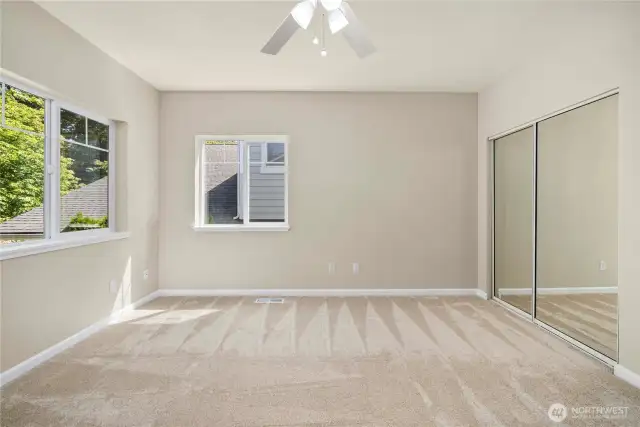 Bright upstairs bedroom with ceiling fan and mirrored closet doors