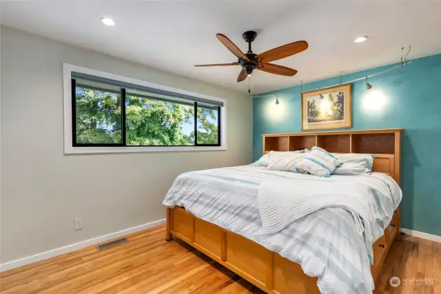 Primary bedroom with ceiling fan, hardwood floors and TV that is remote from ceiling