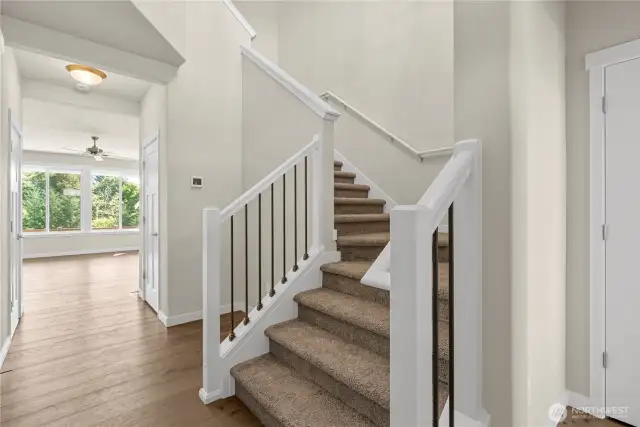 Welcoming entry way with carpeted stairs, elegant white trim and a view to the bright living area with large windows.