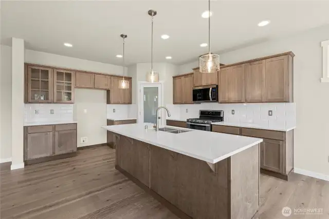 Modern kitchen featuring large center island with sink, quartz counters & eating bar.