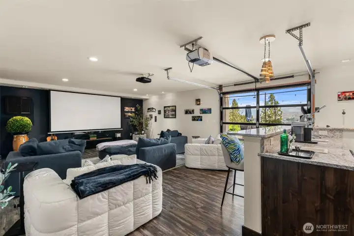 Ultimate entertaining space featuring a home theater, an abundance of seating, and a glass garage door opening to the pool, bocce ball court, patios, and luxurious lounge chairs. Indoor/outdoor entertaining at its best!