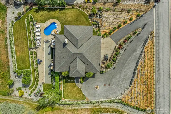 This aerial view showcases the incredible outdoor living — expansive patios, pool, bocce ball court, garden terraces, lush lawn, vineyard setting, parking and exceptional privacy surrounding this luxury Lake Chelan property.