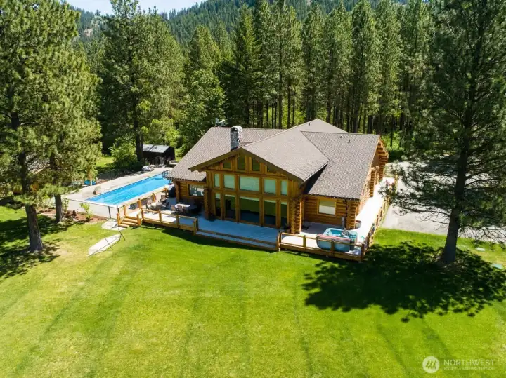 Private retreat surrounded by towering pines, featuring an expansive lawn, pool, and multiple outdoor living areas.